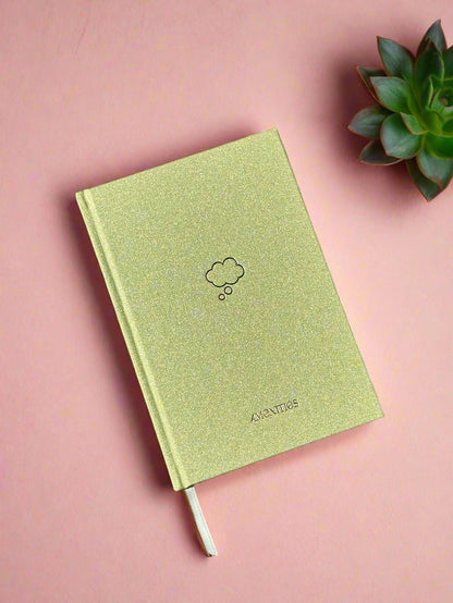 shimmery green notebook with minimalistic gold thought bubble icon on a pink background with a succulent